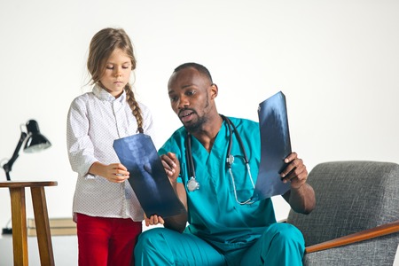 Young afro male pediatrician explaining X-ray to child at clinic. The doctor, health, medicine, patient, pediatrician, illness conceptsの写真素材