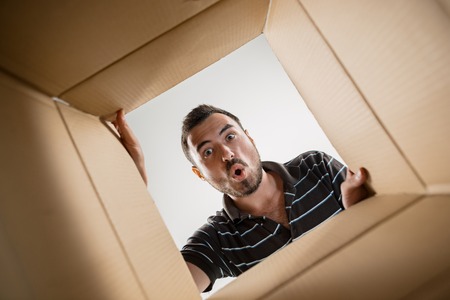 The surprised man unpacking, opening carton box and looking inside. The package, delivery, surprise, gift lifestyle conceptの写真素材