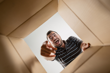 Man smiling, unpacking, opening carton box and looking inside. The package, delivery, surprise, gift lifestyle conceptの写真素材