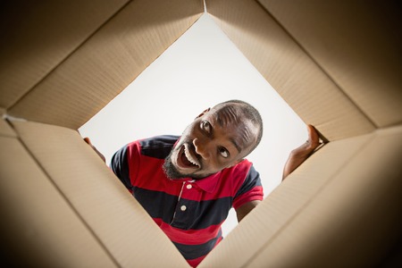 The surprised afrocan man unpacking, opening carton box and looking inside. The package, delivery, surprise, gift lifestyle concept. Human emotions and facial expressions conceptsの写真素材