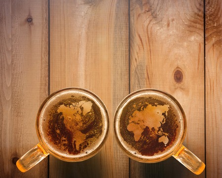 The top view of world map silhouette on foam in beer glass on wooden table. The national love of beer concept