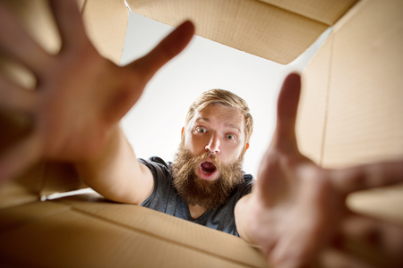 The surprised man unpacking, opening carton box and looking inside. The package, delivery, surprise, gift lifestyle concept. Human emotions and facial expressions conceptsの写真素材