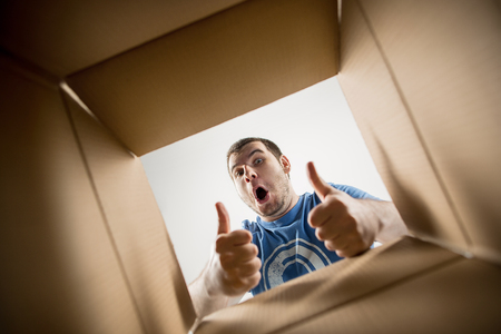 The surprised man unpacking, opening carton box and looking inside. The package, delivery, surprise, gift lifestyle concept. Human emotions and facial expressions conceptsの写真素材
