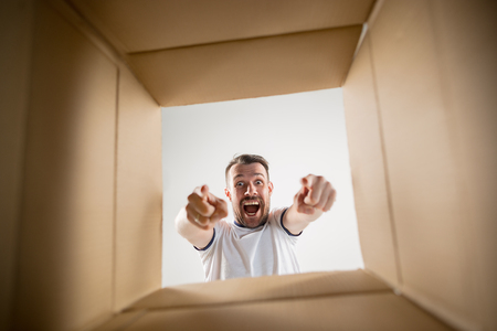 The surprised man unpacking, opening carton box and looking inside. The package, delivery, surprise, gift lifestyle concept. Human emotions and facial expressions conceptsの写真素材