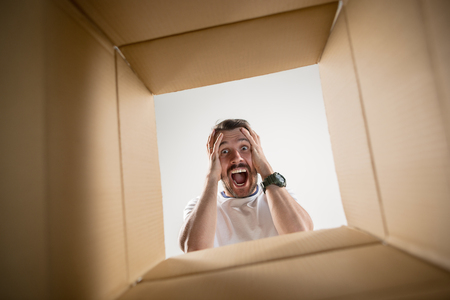 The surprised man unpacking, opening carton box and looking inside. The package, delivery, surprise, gift lifestyle concept. Human emotions and facial expressions conceptsの写真素材