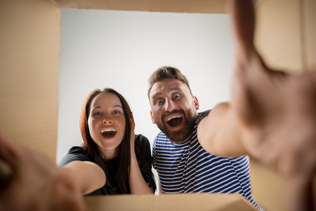 The surprised man and woman unpacking, opening carton box and looking inside. The package, delivery,...
