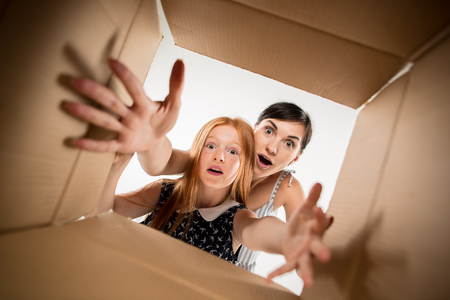 The surprised mom and daughter unpacking, opening carton box and looking inside. The package, delivery, surprise, gift lifestyle concept. Human emotions and facial expressions conceptsの写真素材