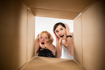 The surprised mom and daughter unpacking, opening carton box and looking inside. The package, delivery, surprise, gift lifestyle concept. Human emotions and facial expressions conceptsの写真素材
