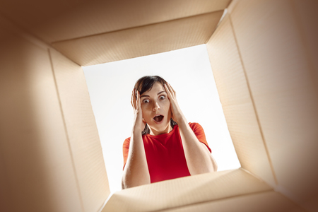 The surprised woman unpacking, opening carton box and looking inside. The package, delivery,...