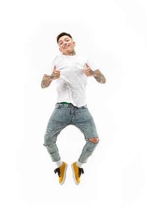 Jump of young man over white studio background using laptop computer while jumping.
