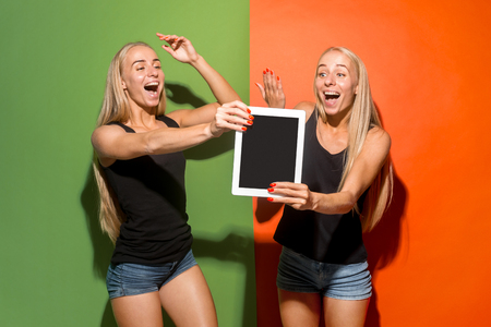 Portrait of a confident casual girls showing blank screen of laptop isolated over colorful studio background.の写真素材