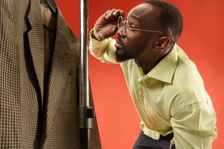Handsome african surprised man with beard choosing shirt in a shop. Concept of shopping and lifestyle. Human emotions conceptsの写真素材