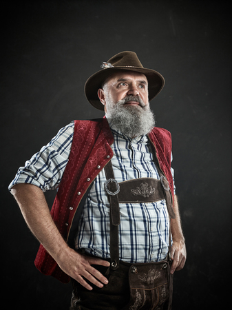 Germany, Bavaria, Upper Bavaria. The smiling man with beer dressed in in traditional Austrian or Bavarian costume in hat holding mug of beer at studioの写真素材