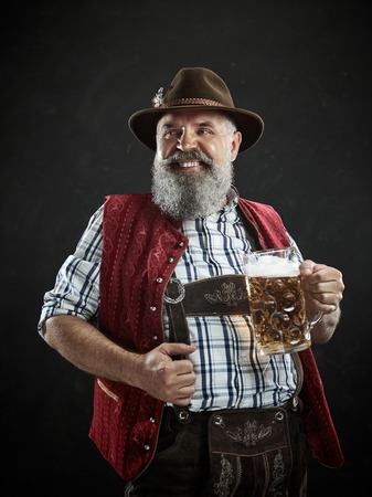 Germany, Bavaria, Upper Bavaria. The smiling man with beer dressed in in traditional Austrian or Bavarian costume in hat holding mug of beer at studioの写真素材