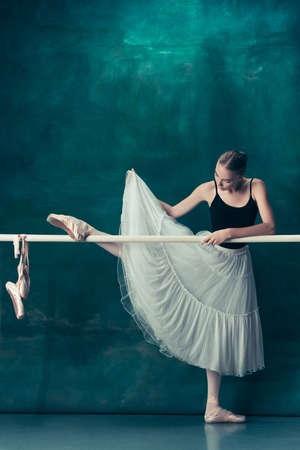 The classic ballet dancer in white tutu posing at ballet barre on studio background. Young teen before dancing. Ballerina project with caucasian model. The ballet, dance, art, contemporary, choreography conceptの写真素材