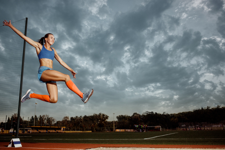 Female athlete performing a long jump during a competition at stadium. The jump, athlete, action, motion, sport, success, championship conceptの素材 [FY310107776811]