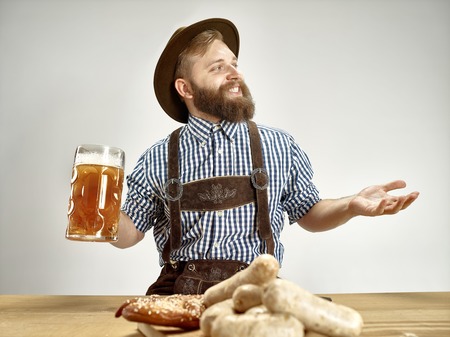 Germany, Bavaria, Upper Bavaria. The young smiling man with beer dressed in traditional Austrian or Bavarian costume in hat holding mug of beer at studioの写真素材