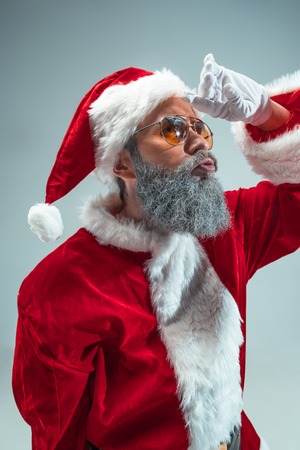 Funny serious guy with christmas hat posing at studio. New Year Holiday. Christmas, x-mas, winter, gifts concept. Man wearing Santa Claus costume on gray. Copy space. Winter sales.の写真素材