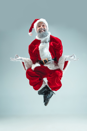 Funny serious guy with christmas hat dancing at studio. New Year Holiday. Christmas, x-mas, winter, gifts concept. Man wearing Santa Claus costume on gray. Copy space. Winter sales.の写真素材