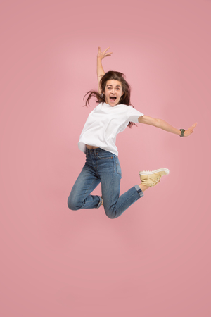 I am happy. Mid-air shot of pretty smiling young woman jumping and gesturing against pink studio background. Runnin girl in motion or movement. Human emotions and facial expressions conceptの写真素材