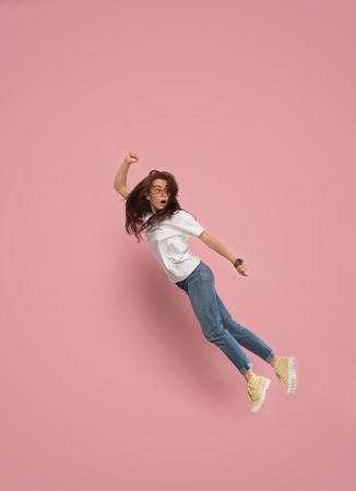 Freedom in moving. Mid-air shot of pretty frightened running away young woman jumping against pink studio background. Runnin girl in motion or movement. Human emotions and facial expressions conceptの写真素材