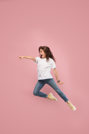 What is there interesting in the distance. seeking pretty happy young woman jumping and grabbing against pink studio background. Runnin girl in motion or movement. Human emotions and facial expressions conceptの写真素材