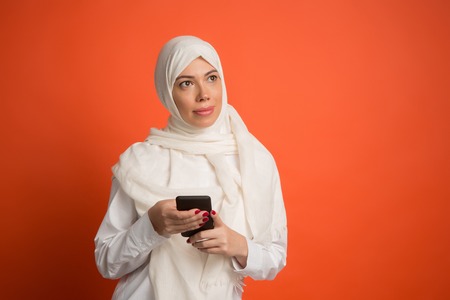 Happy arab woman in hijab with mobile phone. Portrait of smiling girl, posing at red studio...