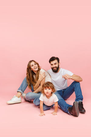 A happy family on pink studio background. The father, mother and son posing togetherの写真素材