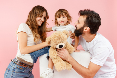A happy family on pink studio background. The father, mother and son posing together with teddy bear toyの写真素材