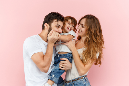 A happy family on pink studio background. The father, mother and son posing togetherの写真素材