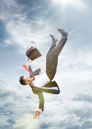 The frightened businessman in suit falling down and screaming against blue sky background.の写真素材