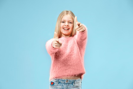 Happy teen girl standing, smiling isolated on trendy blue studio background. Beautiful female portrait. Young satisfy girl with sign ok. Human emotions, facial expression concept. Front view.の写真素材