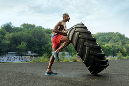 Handsome african american muscular man flipping big tire outdoor.の写真素材