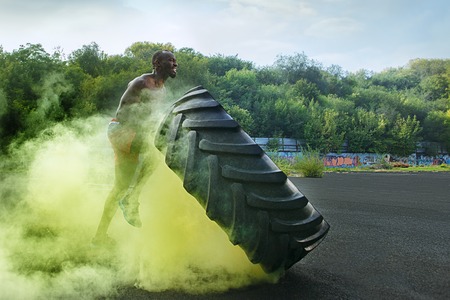 Handsome african american muscular man flipping burning big tire outdoor with smokeの写真素材