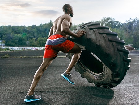 Handsome african american muscular man flipping big tire outdoor.の写真素材