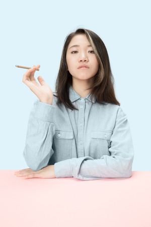 Handsome young korean women smoking cigar while sitting at table at studio. Trendy colorsの写真素材