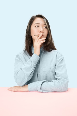 Handsome young korean women smoking cigar while sitting at table at studio. Trendy colorsの写真素材