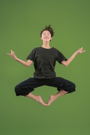 Mid-air shot of pretty smiling young woman jumping and gesturing against green studio background....