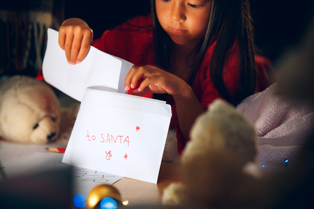 Merry Christmas and Happy Holidays. Cute little child girl writes the letter to Santa Claus near Christmas tree at home indoor. The holiday, childhood, winter, celebration conceptの写真素材