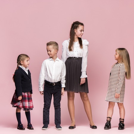 Cute smiling happy stylish children on pink background. Beautiful stylish teen girls and boy standing together and posing at studio. Classic style. Kids fashion and emotions concept.の写真素材