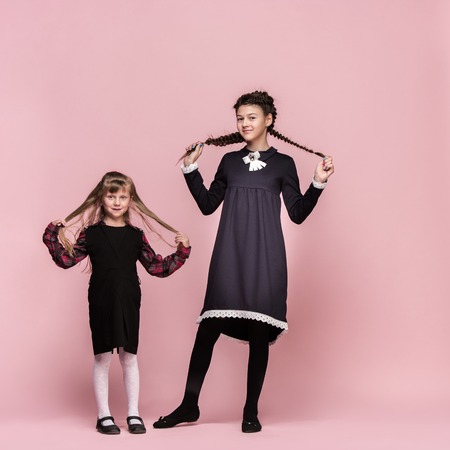 Cute smiling happy stylish children on pink background. Beautiful stylish teen girls standing together and posing at studio. Classic style. Kids fashion and emotions concept.の写真素材