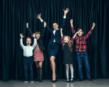 Cute smiling happy stylish children and female teacher on dark background. Beautiful stylish teen...