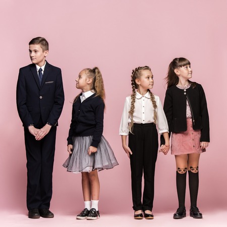 Cute smiling surprised stylish children on pink background. Beautiful stylish teen girls and boy standing together and posing at studio. Classic style. Kids fashion and emotions concept.の写真素材
