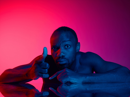Close up portrait of a young naked african man looking at camera while standing indoors. High Fashion male model in colorful bright lights posing in studio. Art design over vivid background.の写真素材