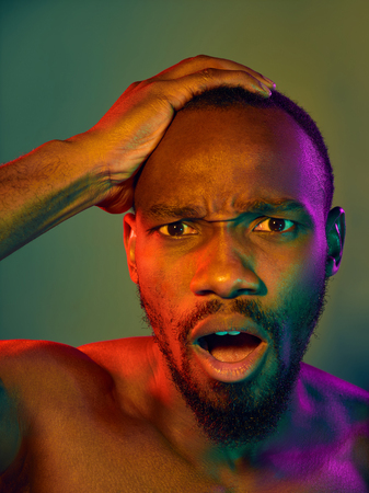 Close up portrait of a young naked happy african man looking at camera. High Fashion male model in colorful bright lights posing in studio. Art design over vivid background.の写真素材