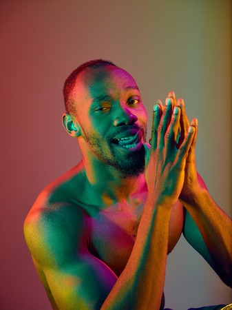Close up portrait of a young naked happy smiling african man looking at camera. High Fashion male model in colorful bright lights posing in studio. Art design over vivid background.の写真素材