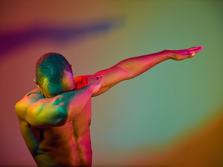 Close up portrait of a young naked happy african man dancing. High Fashion male model in colorful bright lights posing in studio. Art design over vivid background.の写真素材