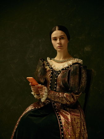 Portrait of a girl wearing a princess or countess dress with mobile phone over dark studioの写真素材