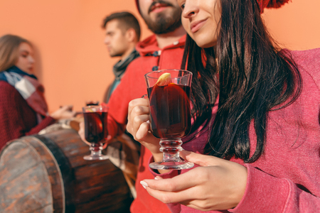 Smiling european men and women during party photoshoot. The guys posing as friends at studio fest with wineglasses with hot mulled wine on foreground.の写真素材