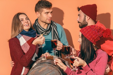 Smiling european men and women during party photoshoot. The guys posing as friends at studio fest with wineglasses with hot mulled wine on foreground.の写真素材